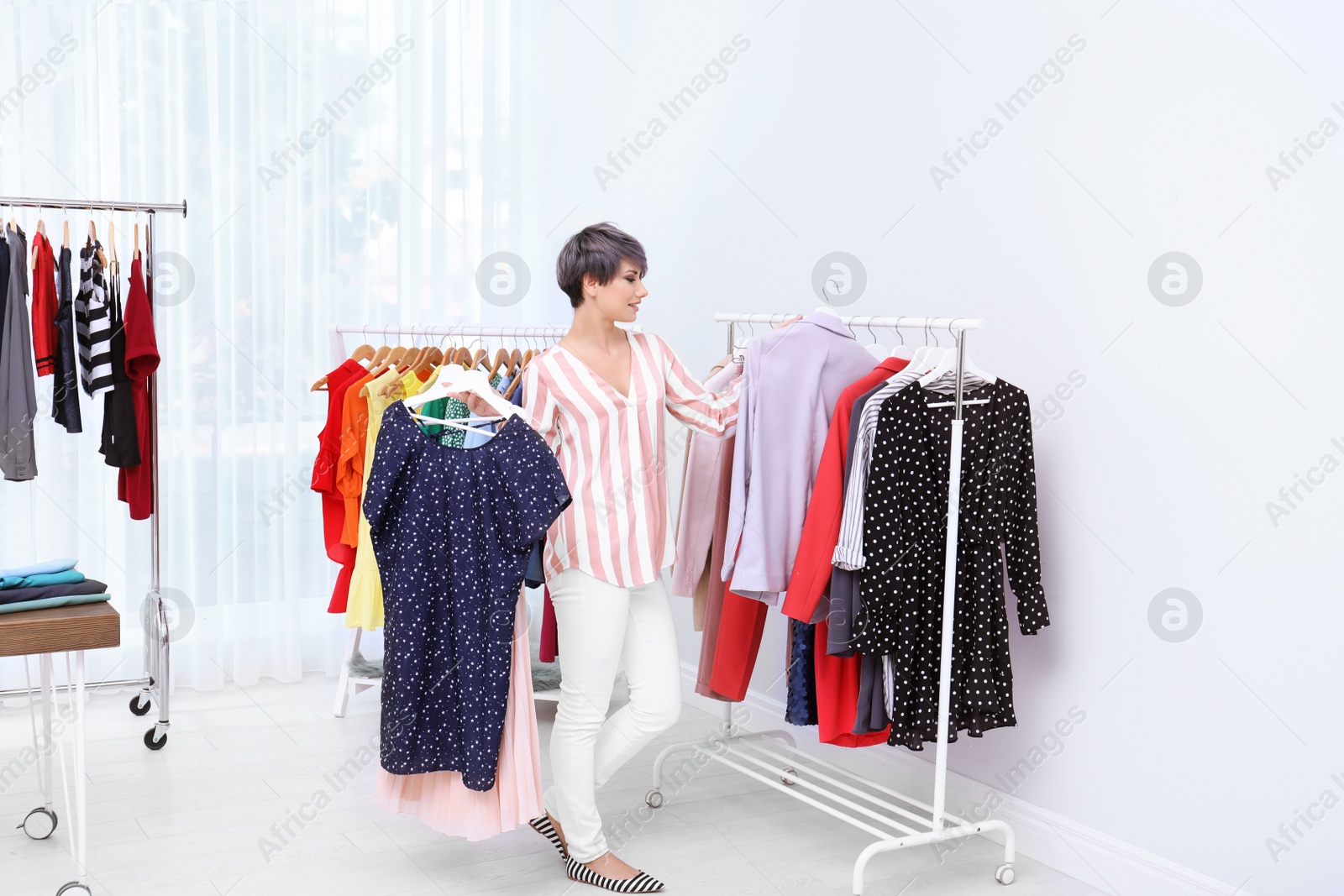 Photo of Beautiful young stylist choosing clothes in studio