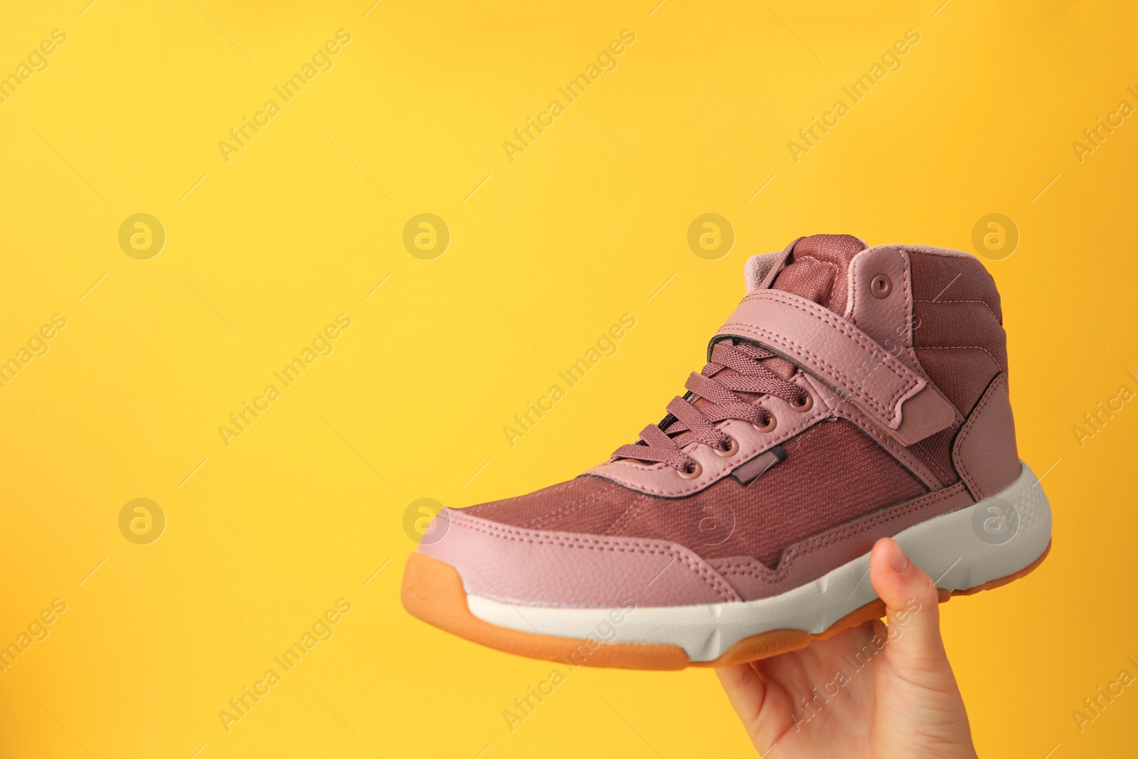 Photo of Girl holding stylish sneaker on yellow background, closeup. Space for text