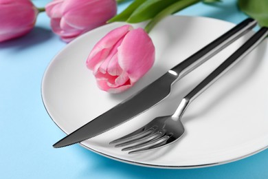 Photo of Stylish table setting with cutlery and tulips on light blue background, closeup