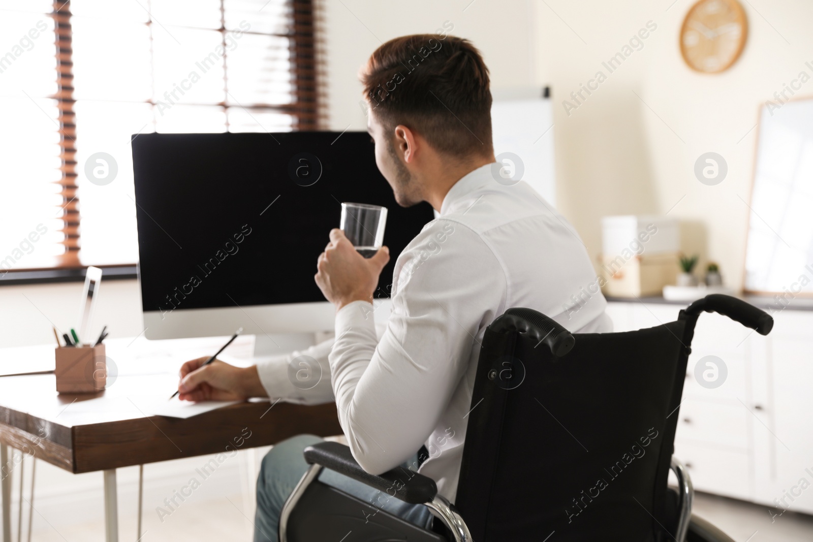 Photo of Man in wheelchair with computer drinking water at workplace. Space for text