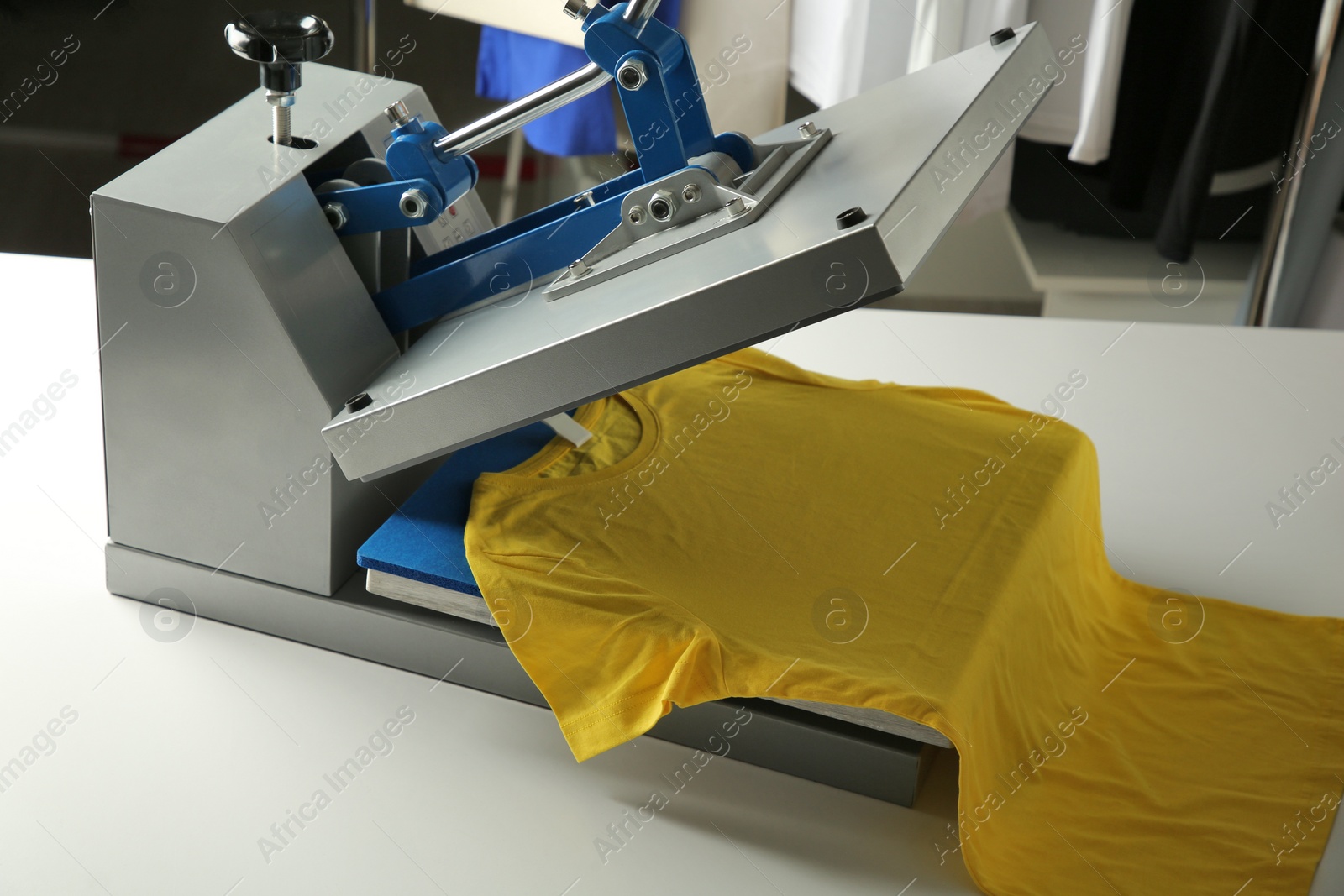 Photo of Printing logo. Heat press with yellow t-shirt on white table