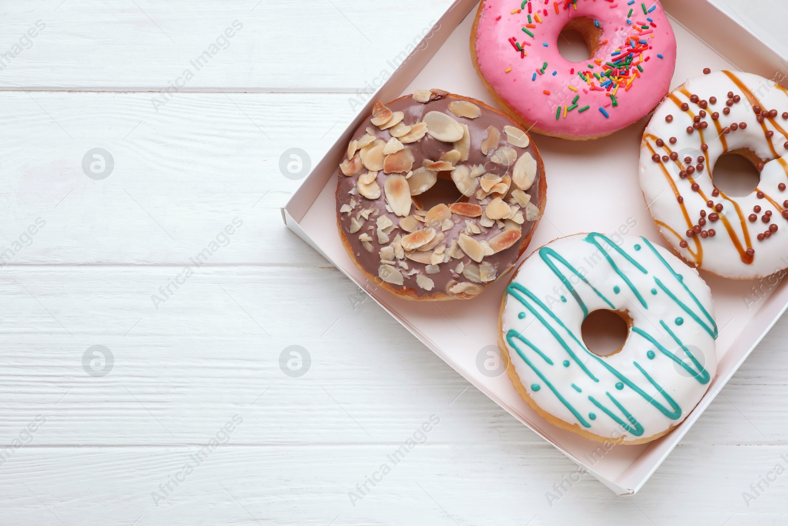 Photo of Box with tasty glazed donuts on white wooden table, top view. Space for text