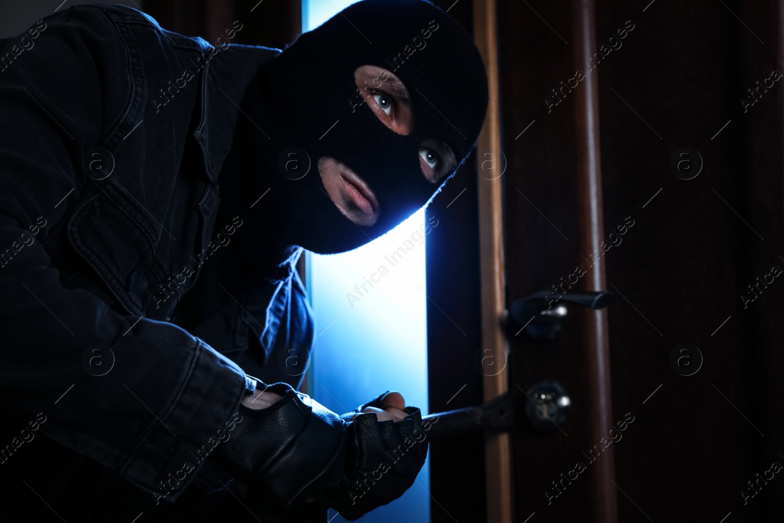 Photo of Man in mask forcing door with crow bar. Dangerous criminal