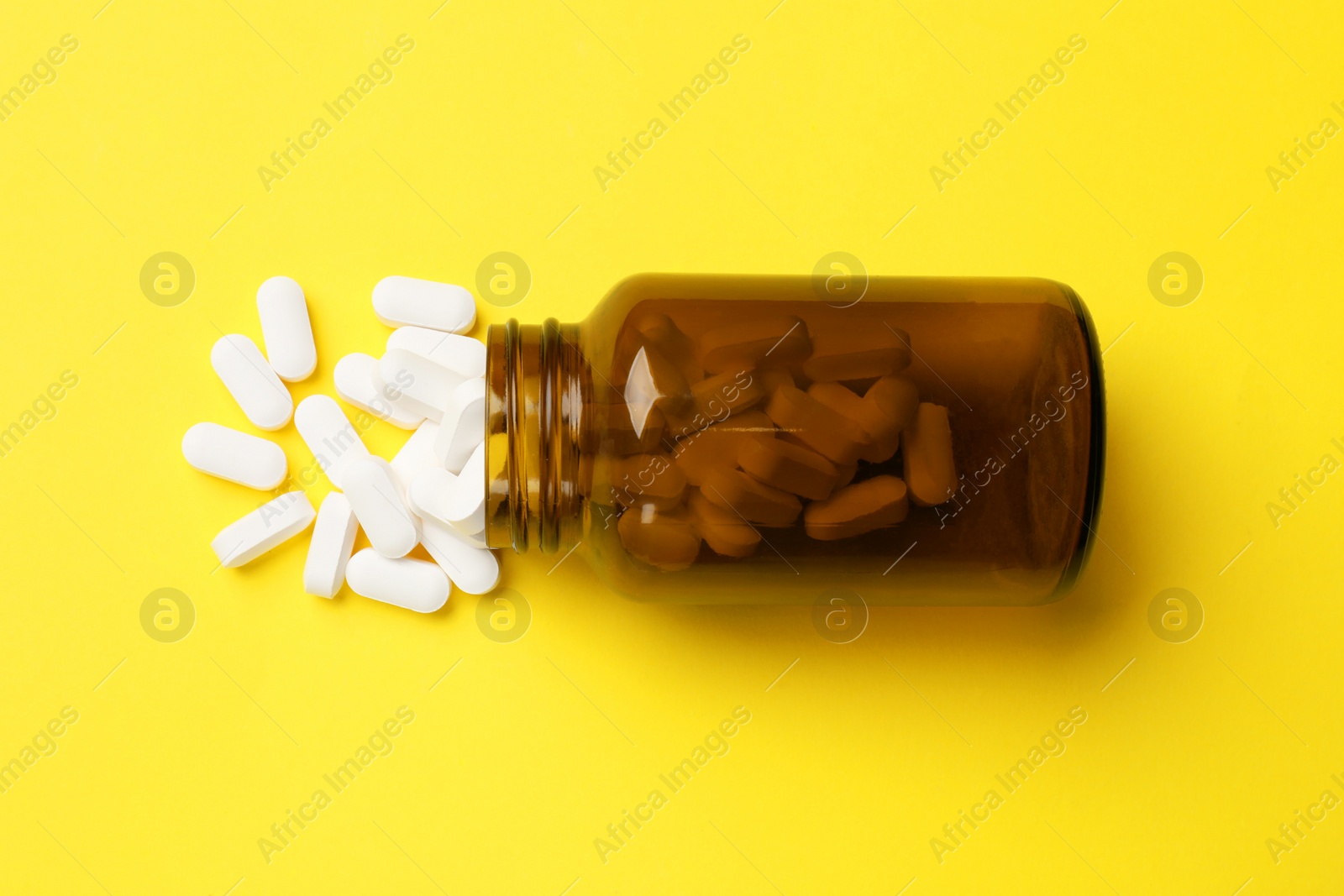 Photo of Vitamin pills and bottle on yellow background, top view