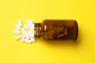 Photo of Vitamin pills and bottle on yellow background, top view