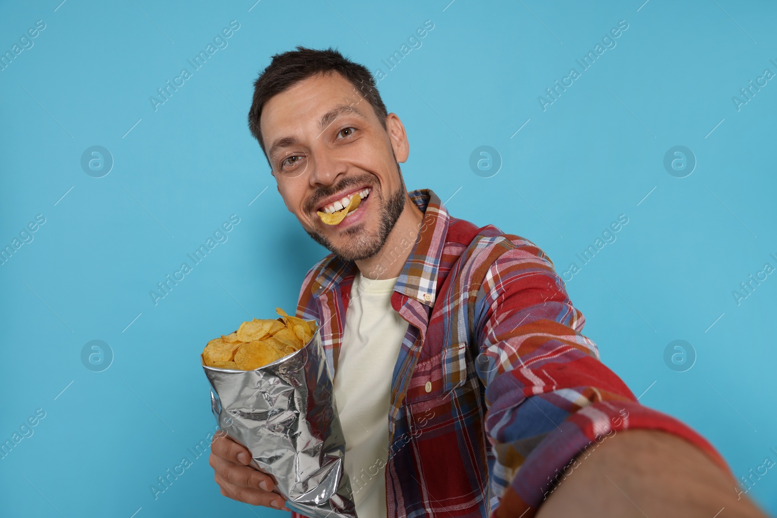 Photo of Handsome man taking selfie with potato chips on light blue background