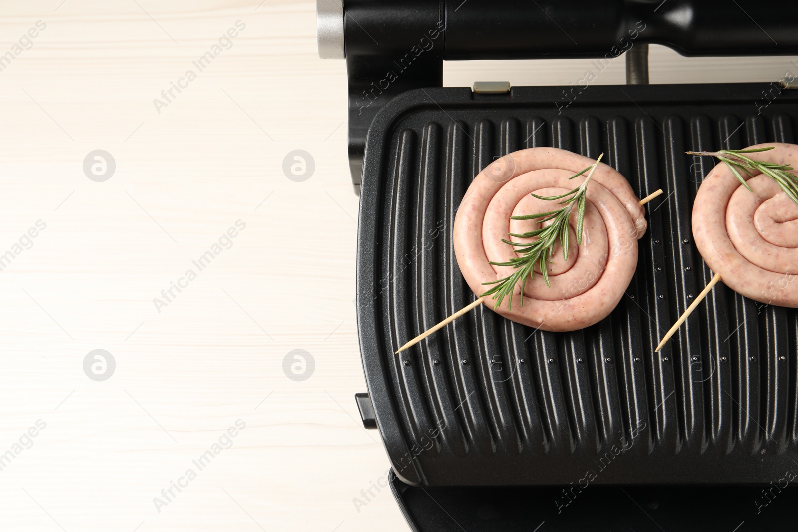 Photo of Electric grill with homemade sausages and rosemary on wooden table, top view. Space for text