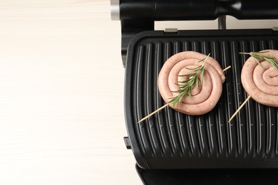 Photo of Electric grill with homemade sausages and rosemary on wooden table, top view. Space for text