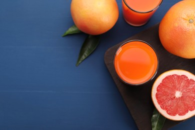 Photo of Tasty grapefruit juice in glasses and fresh fruits on blue wooden table, flat lay. Space for text