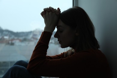Photo of Sad young woman near window at home