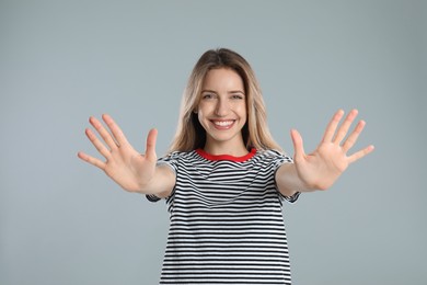 Photo of Woman showing number ten with her hands on light grey background