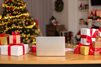 Photo of Modern laptop and Christmas gifts on table at home