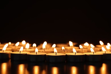 Photo of Burning candles on dark surface against black background, closeup. Space for text