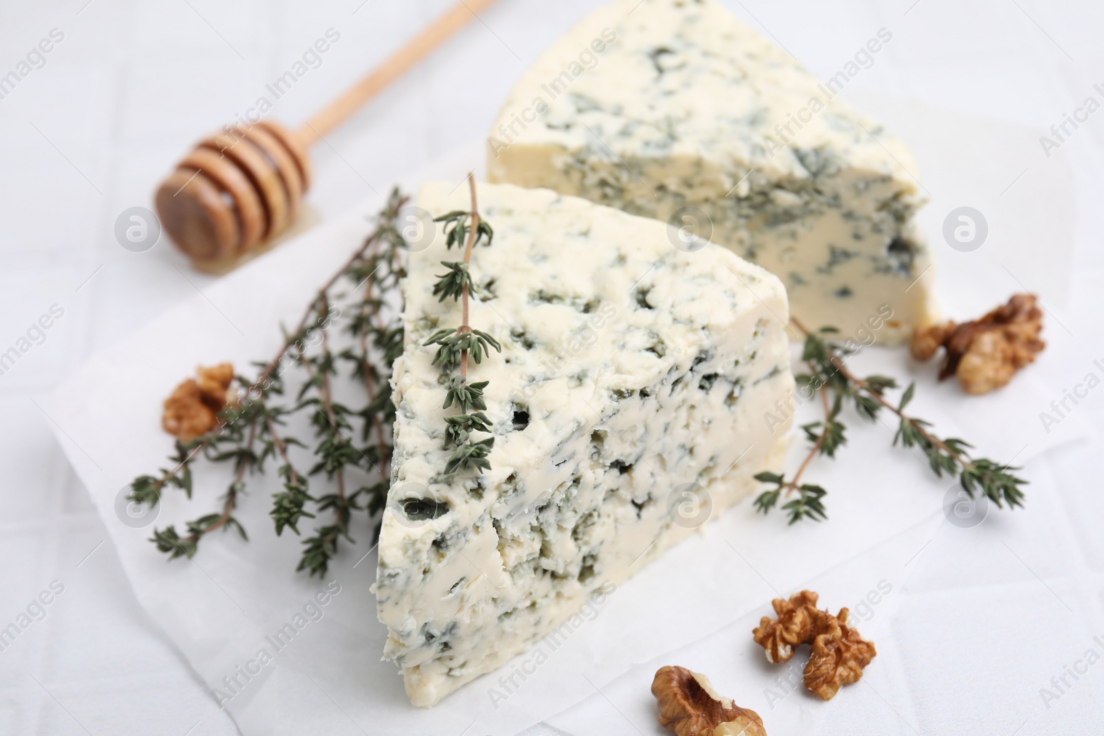 Photo of Tasty blue cheese with thyme, walnuts and honey dipper on white table, closeup