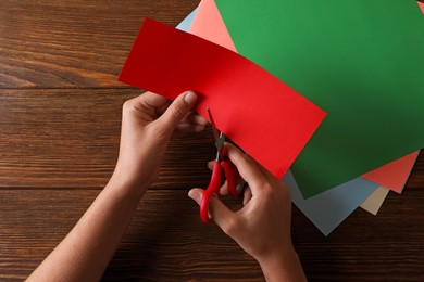 Photo of Woman cutting red paper with scissors at wooden background, top view