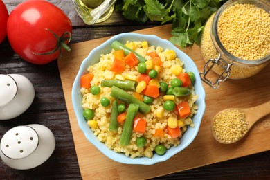 Photo of Tasty millet porridge with vegetables in bowl and products on wooden table, flat lay