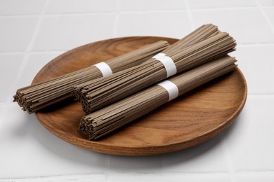 Uncooked buckwheat noodles (soba) on white tiled table, closeup