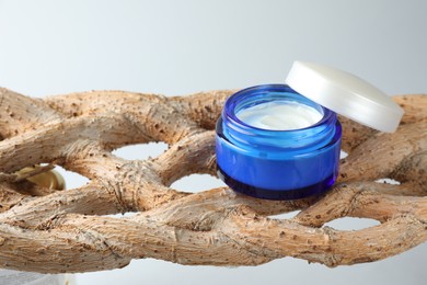 Photo of Open jar with moisturizing cream on wooden branch against light grey background