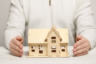 Photo of Home security concept. Man with house model at white wooden table, closeup