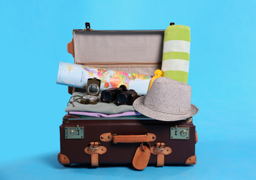 Photo of Open vintage suitcase with clothes packed for summer vacation on light blue background