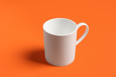 Photo of One white ceramic mug on orange background