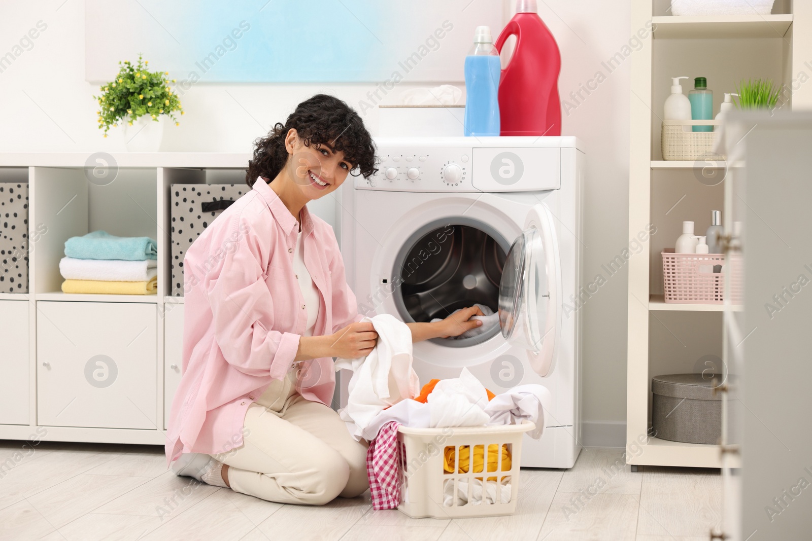 Photo of Happy woman putting laundry into washing machine indoors