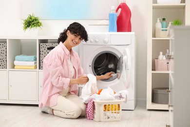 Happy woman putting laundry into washing machine indoors