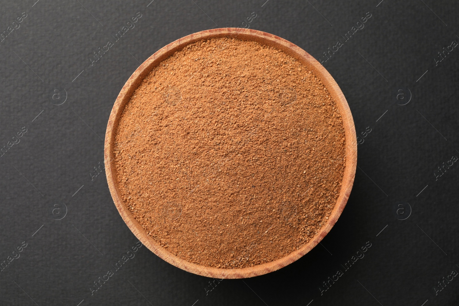 Photo of Wooden bowl with aromatic cinnamon powder on grey background