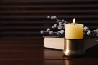 Photo of Burning candle, Bible and willow branches on wooden table, closeup. Space for text