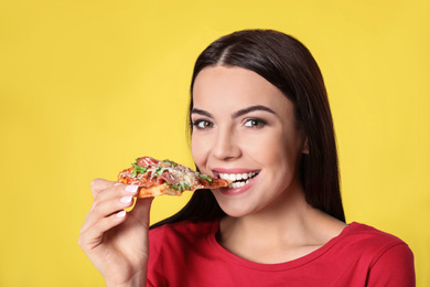 Beautiful woman eating tasty pizza on yellow background