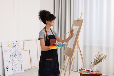 Photo of Young woman painting on easel with paper in studio