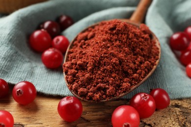 Photo of Spoon with cranberry powder and fresh berries on wooden table, closeup