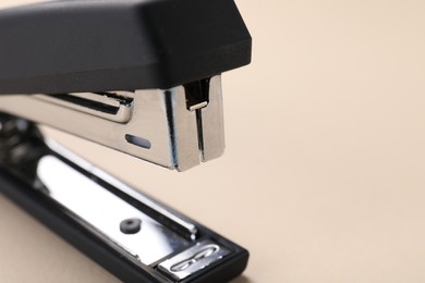 Black stapler s on beige background, closeup. Space for text