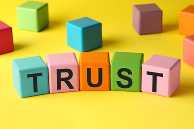 Photo of Word Trust made of colorful cubes on yellow background