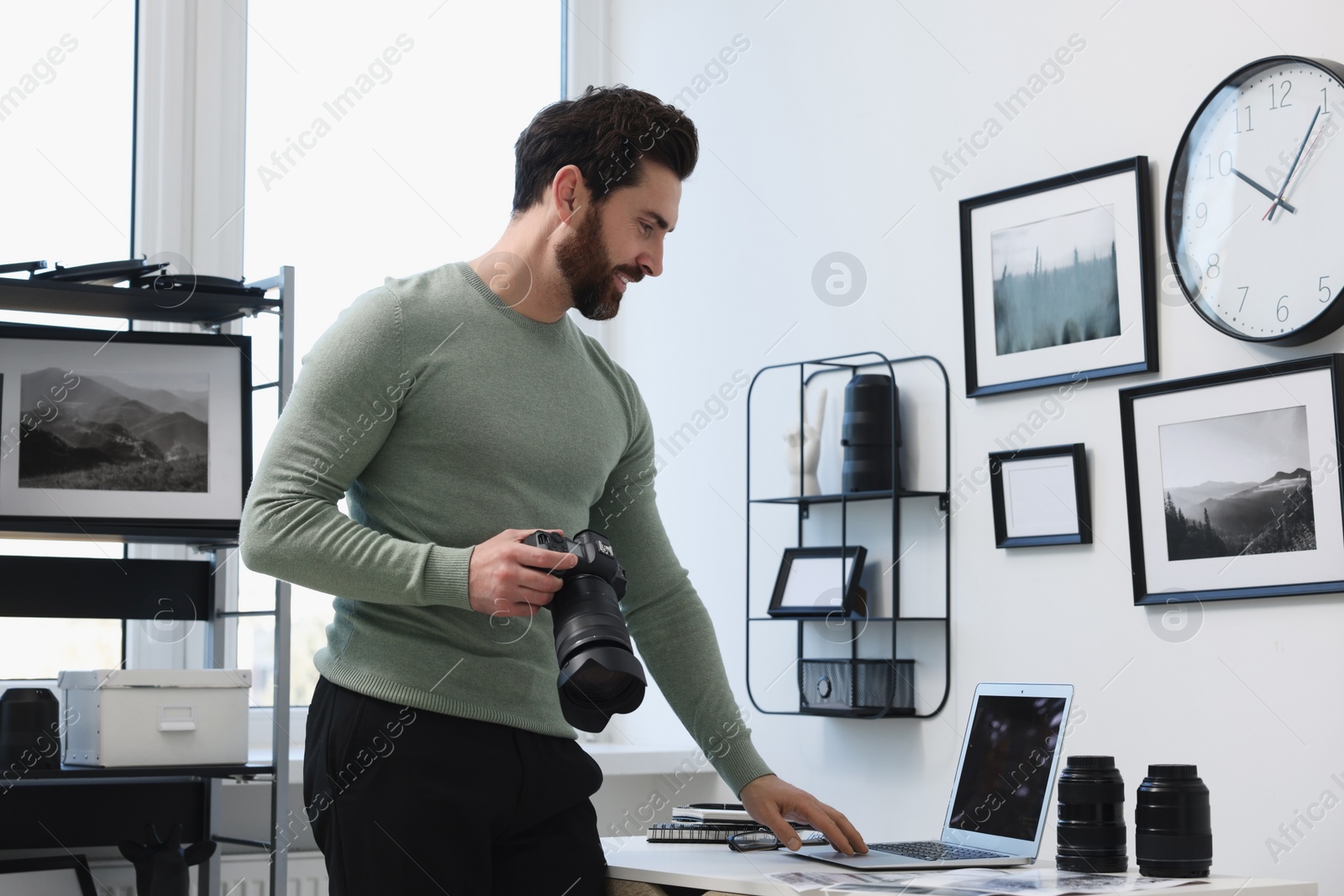 Photo of Professional photographer with digital camera using laptop in office