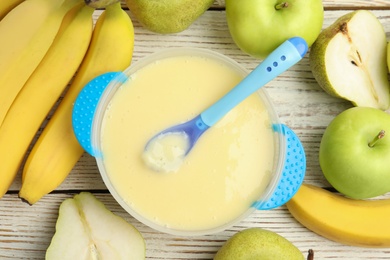 Baby food in bowl and fresh ingredients on white wooden table, flat lay