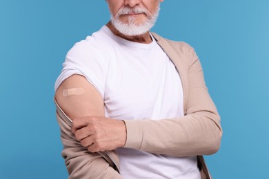 Photo of Man with adhesive bandage on his arm after vaccination against light blue background, closeup