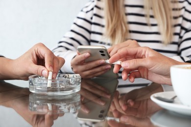 Photo of Woman putting out cigarette in ashtray at table, closeup