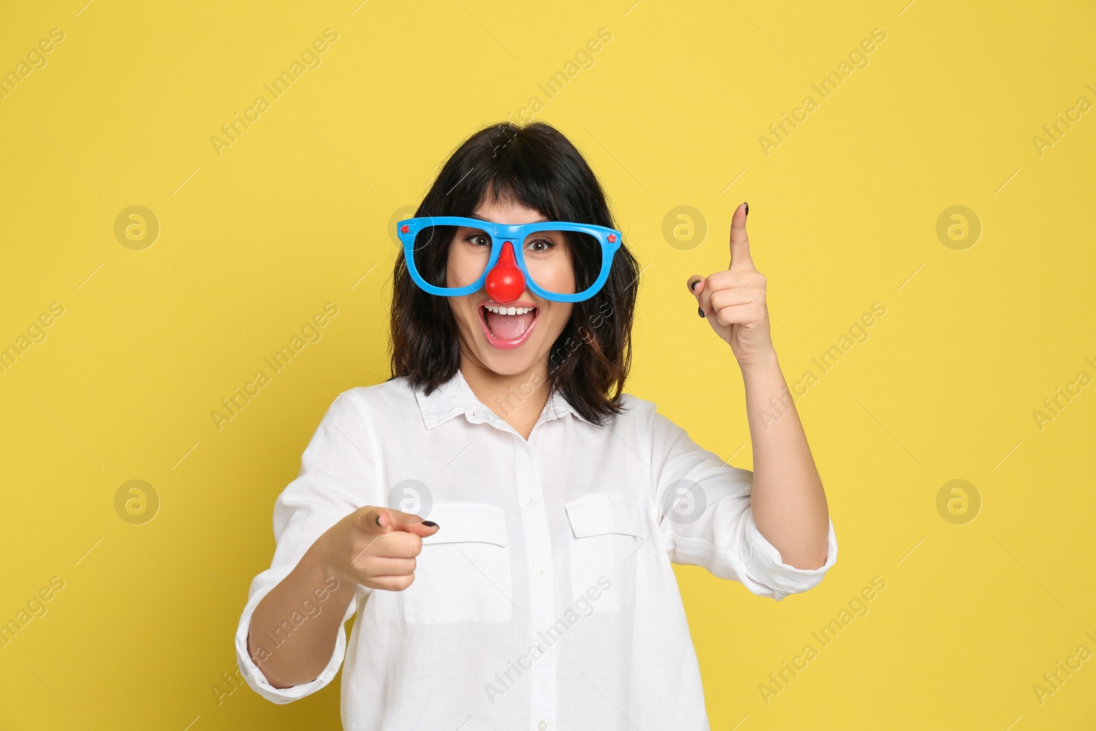 Photo of Joyful woman with funny glasses on yellow background. April fool's day