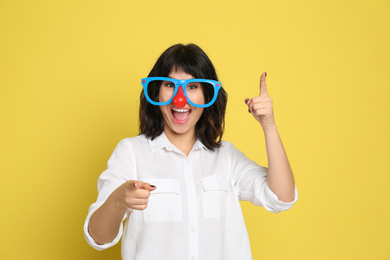 Joyful woman with funny glasses on yellow background. April fool's day