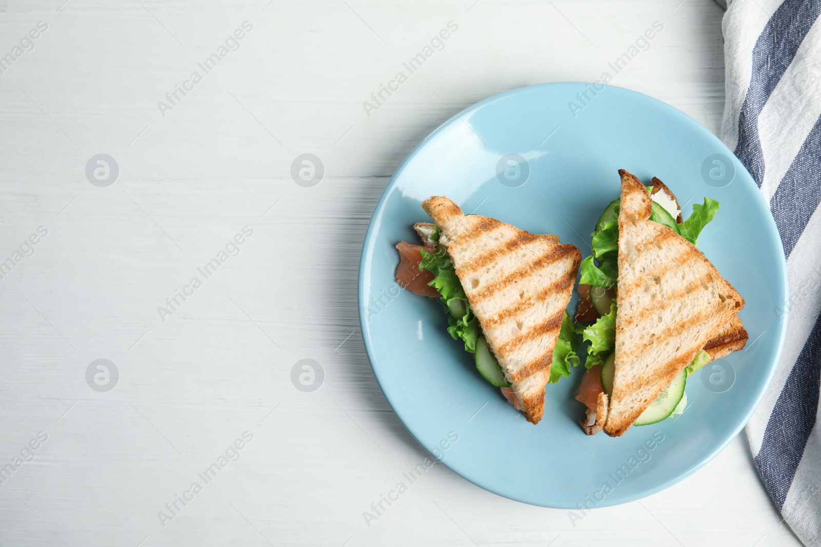 Photo of Blue plate with tasty sandwiches on white table, top view. Space for text