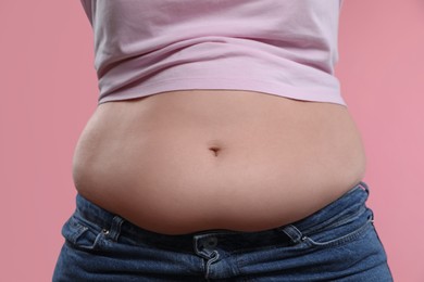 Woman with excessive belly fat on pink background, closeup. Overweight problem
