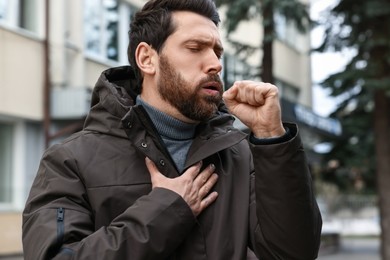 Sick man coughing on city street. Cold symptoms