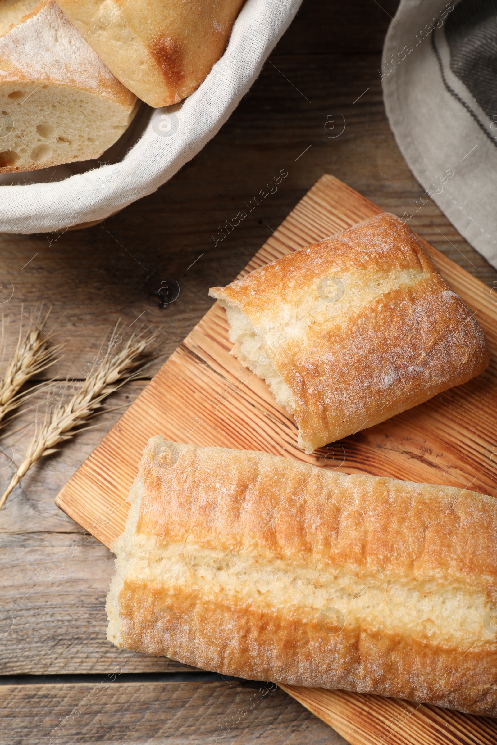 Photo of Broken tasty baguette and spikelets on wooden table, flat lay