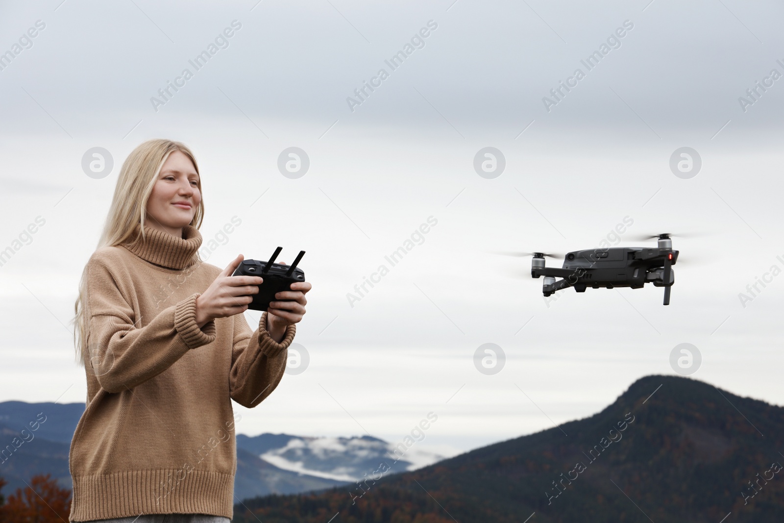 Photo of Young woman operating modern drone with remote control in mountains