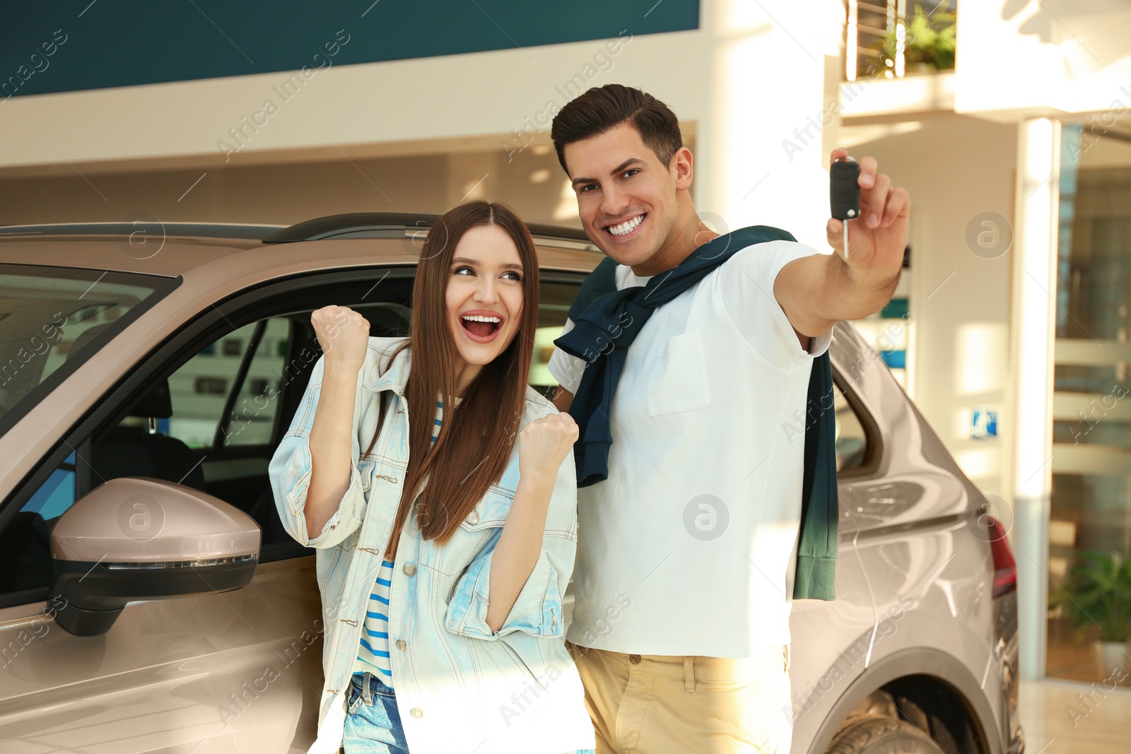 Photo of Happy couple with car key in modern auto dealership