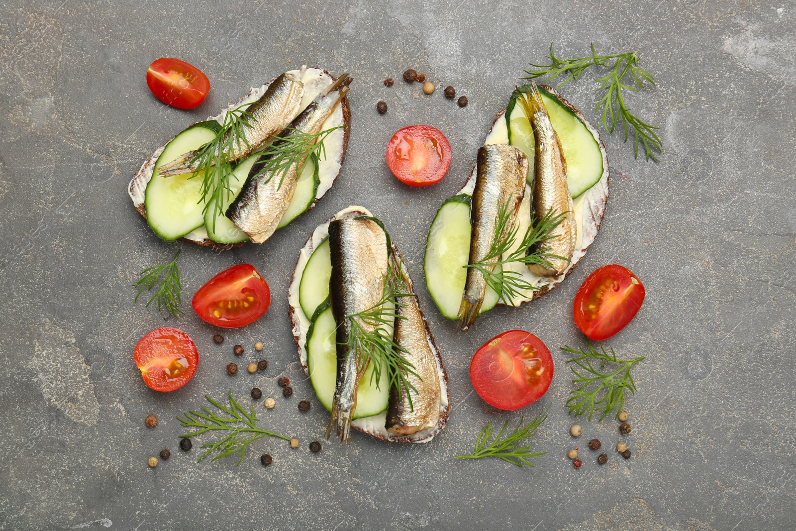 Delicious sandwiches with sprats, cucumber and dill served on grey table, flat lay Photo of Delicious sandwiches with sprats, cucumber and dill served on grey table, flat lay