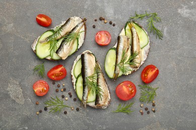 Photo of Delicious sandwiches with sprats, cucumber and dill served on grey table, flat lay