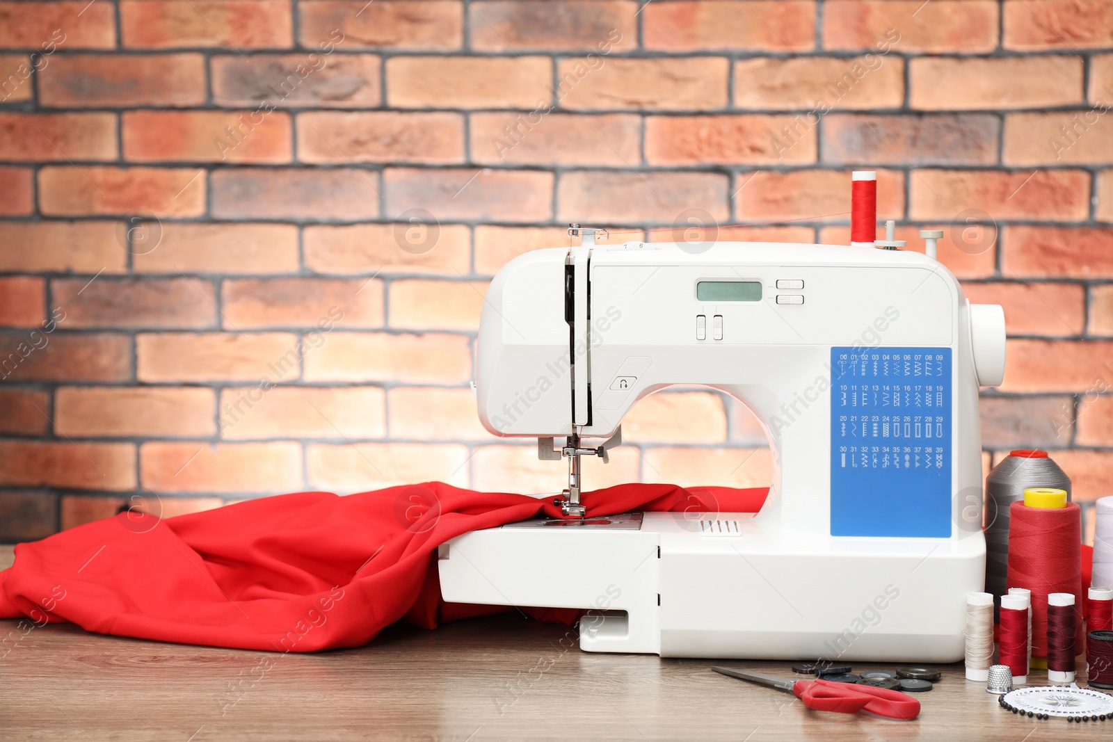 Photo of Sewing machine with fabric and craft accessories on wooden table against brick wall