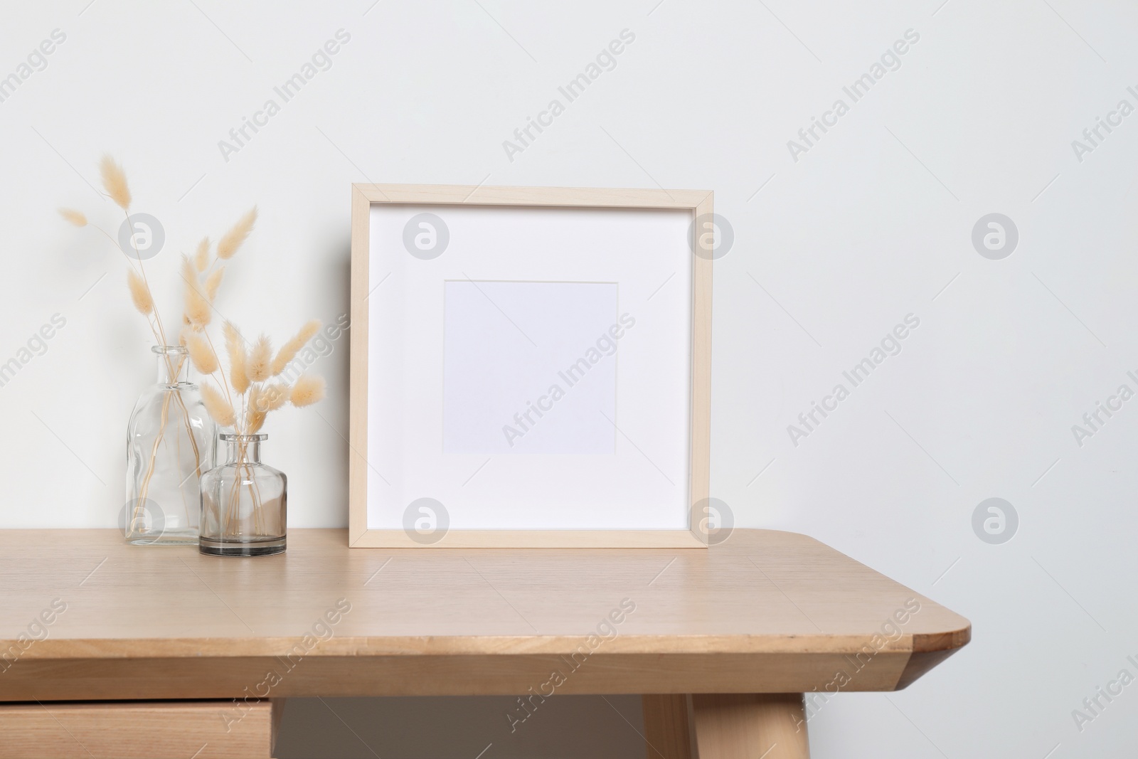 Photo of Empty photo frame and vases with dry decorative spikes on wooden table. Mockup for design